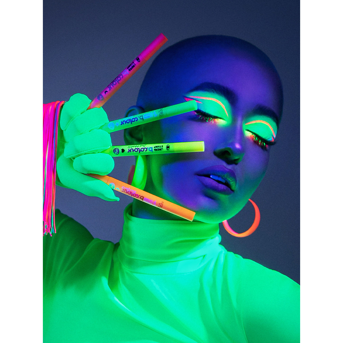 Modell in Neon-Look mit leuchtendem Make-up, das vier b.colour Eyeliner in Neonfarben (Orange, Gelb, Grün und Pink) präsentiert.