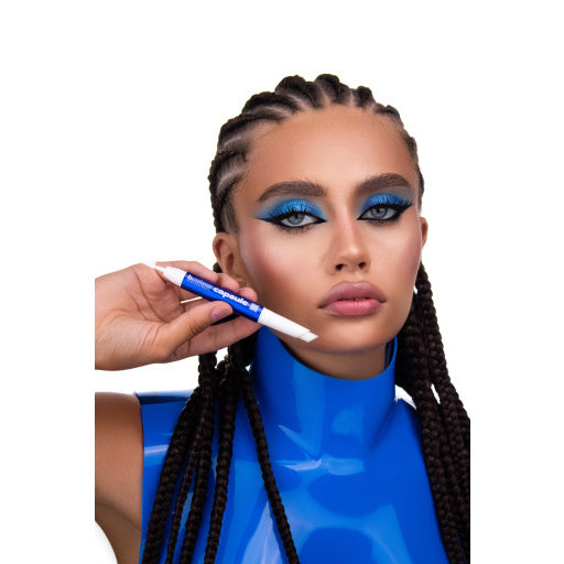 Model mit geflochtenen Haaren und intensiv blauem Augen-Make-up hält den b.colour Professional Capsule Super Fixing Brow Wax in Stiftform neben ihrem Gesicht.