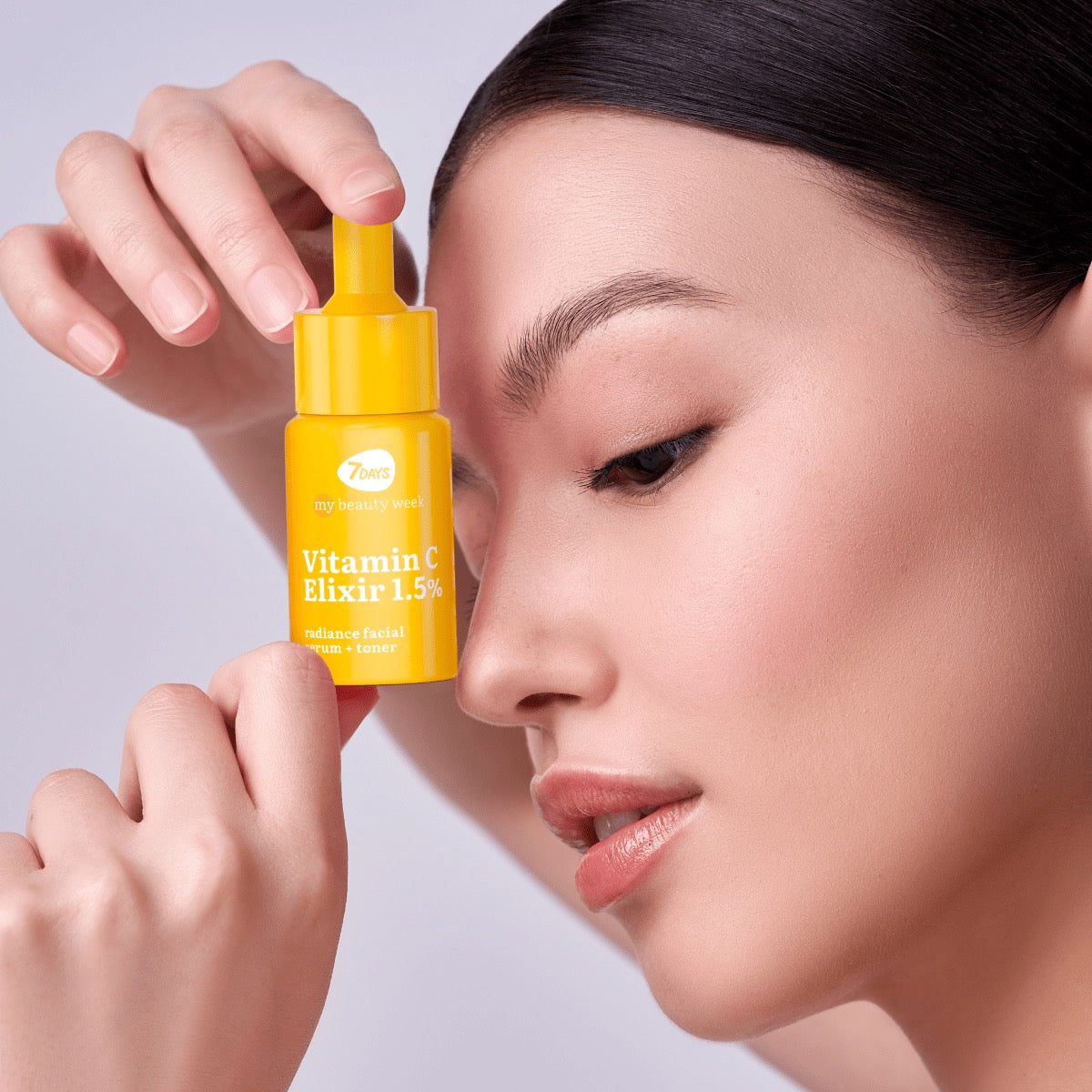 Nahaufnahme einer Frau, die eine gelbe Pipettenflasche 7DAYS my beauty week Vitamin C Elixir 1,5% Radiance Facial Serum + Toner an ihre Schläfe hält.
