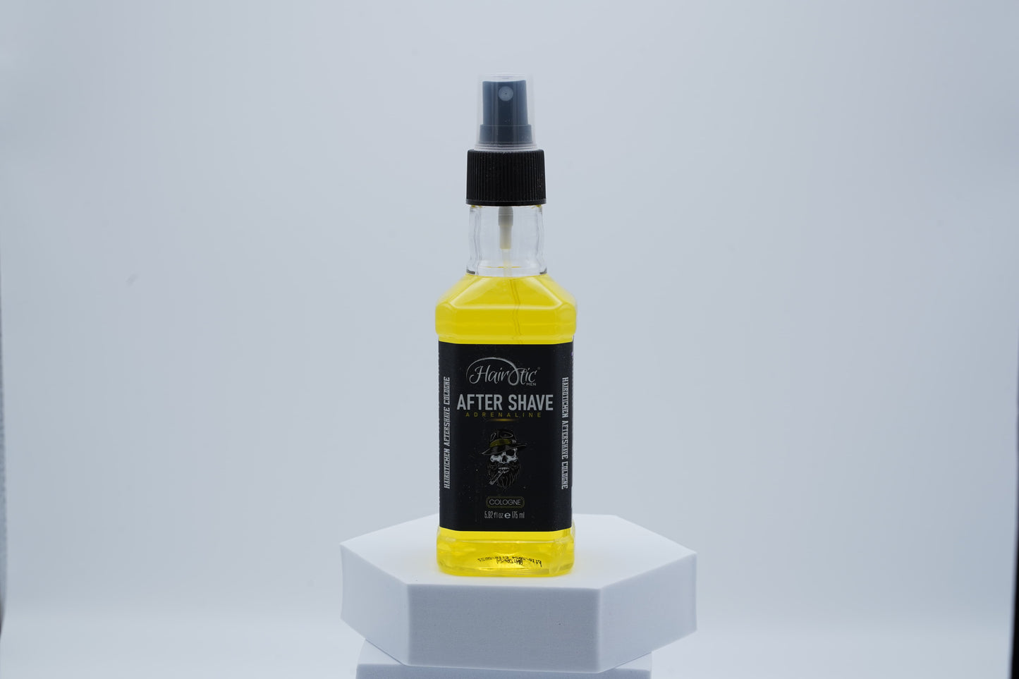 Gelbe Sprühflasche Hairotic After Shave Adrenaline, mit schwarzem Etikett und Totenkopf-Logo, auf weißem Podest vor neutralem Hintergrund.
