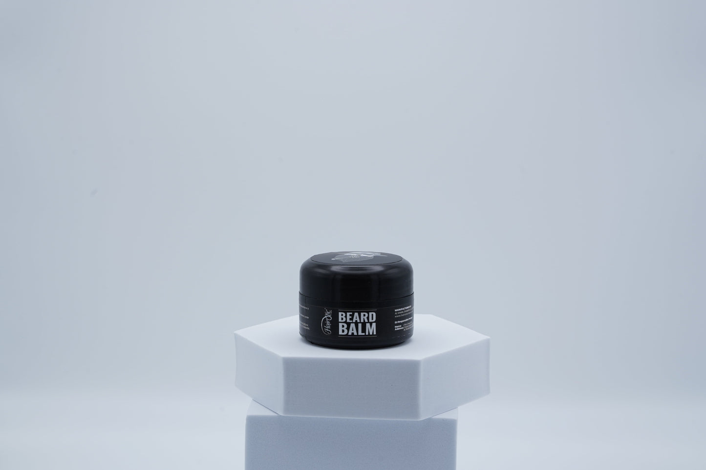 Schwarze Dose Hairotic Beard Balm mit weißem Schriftzug, platziert auf weißem Podest vor neutralem Hintergrund.