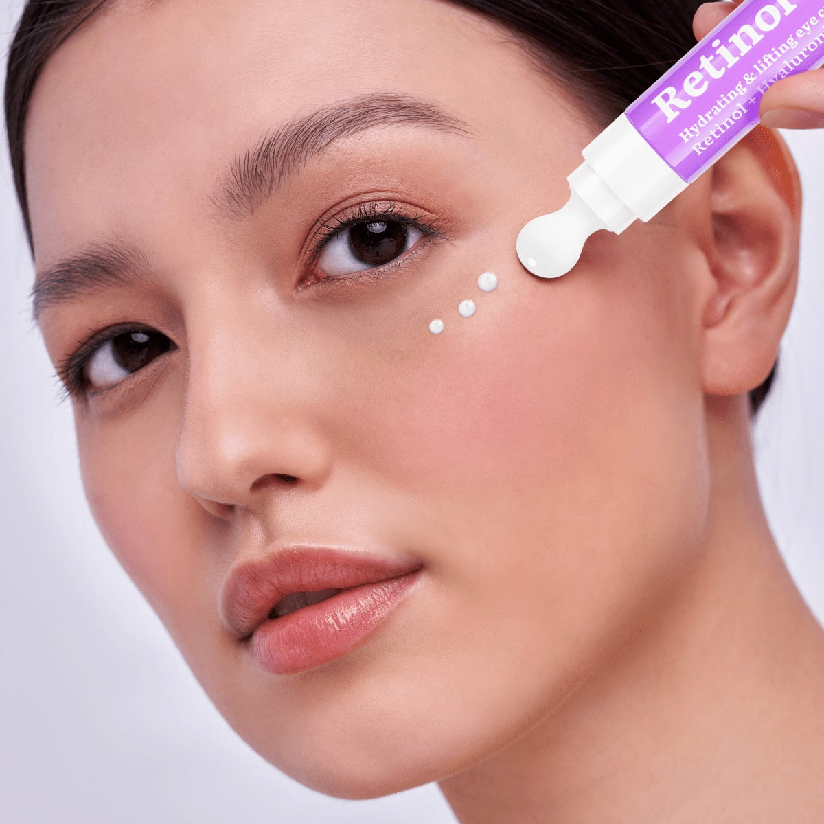 Frau trägt eine Augencreme mit Retinol aus einem Applikator im Tubenformat punktuell unter dem Auge auf, Nahaufnahme der Gesichtspartie mit Fokus auf die Hautpflege-Routine.