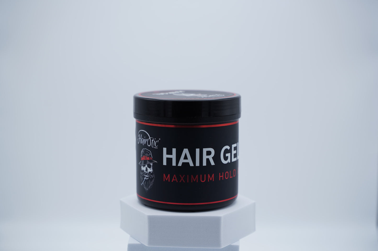 Schwarze Dose Hairotic Hair Gel Maximum Hold mit rotem Akzentdesign, starke Stylingkontrolle, auf weißem Podest vor neutralem Hintergrund.