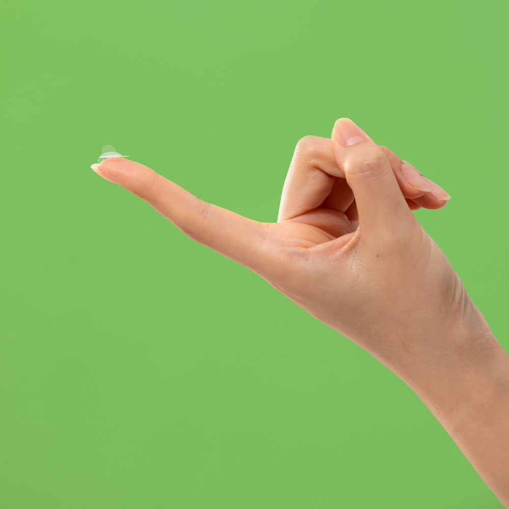 Troubless Invisible Spot Patch – durchsichtiges Pickelpatch auf Fingerspitze vor grünem Hintergrund