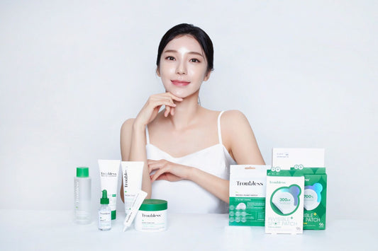 Frau mit klarer Haut präsentiert Troubless Hautpflegeprodukte, darunter Reinigungsgel, Toner, Serum, Creme und Spot Patches.