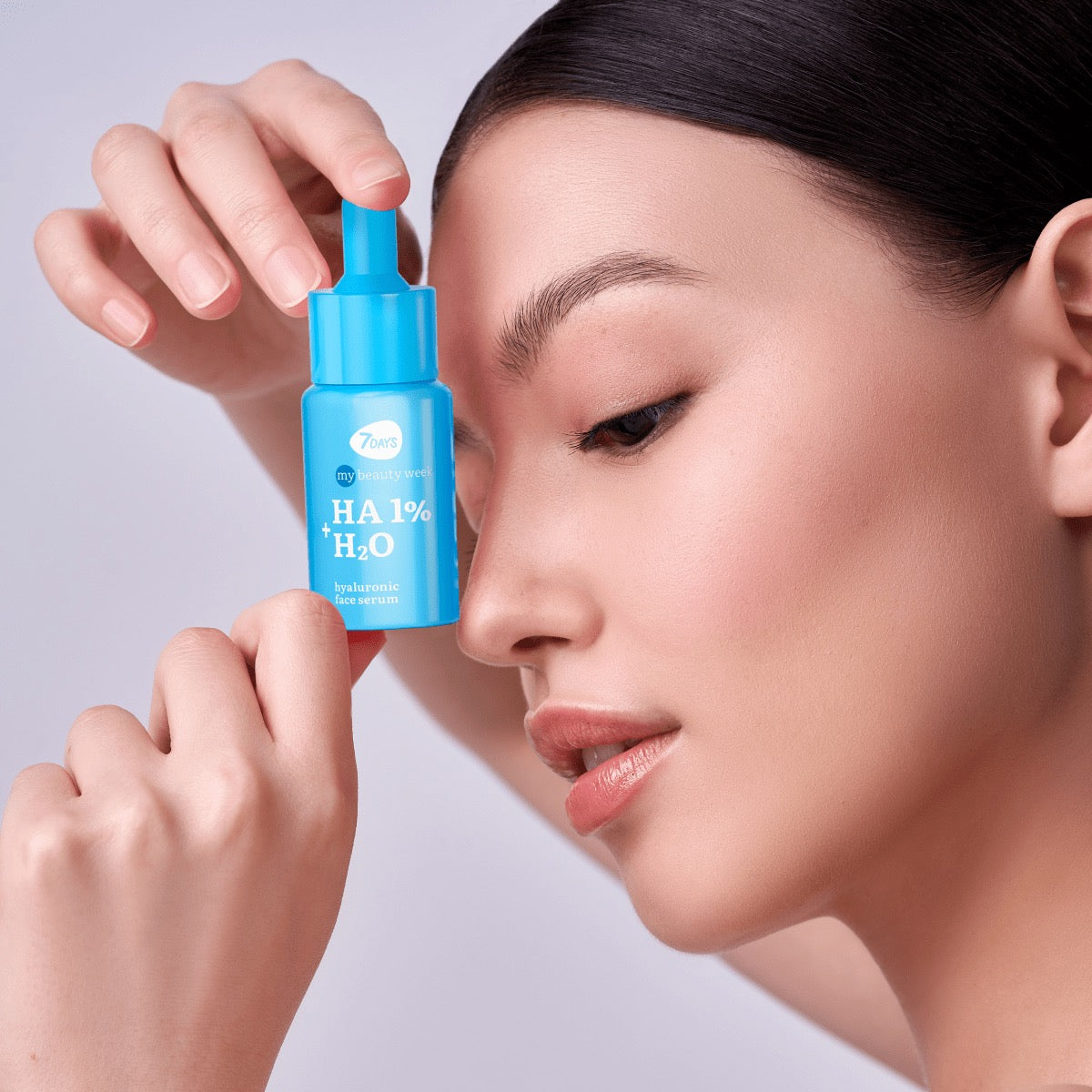 Nahaufnahme einer Frau, die eine blaue Pipettenflasche 7DAYS my beauty week HA 1% + H₂O Hyaluronic Face Serum neben ihrem Gesicht hält.