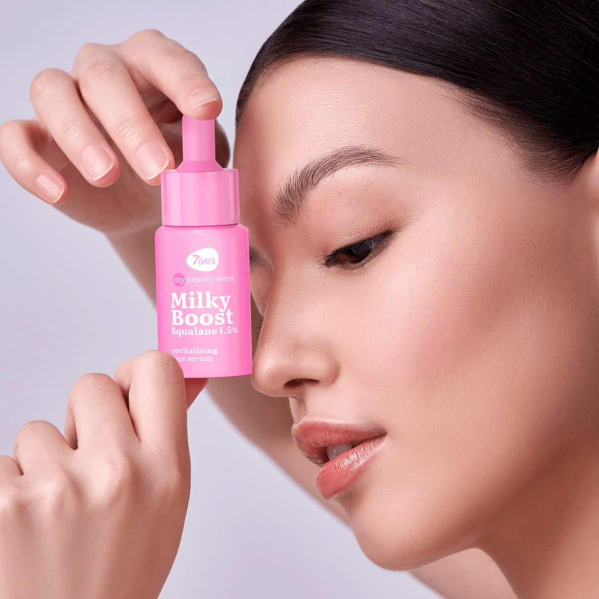 Nahaufnahme einer Frau, die eine pinke Pipettenflasche 7DAYS my beauty week Milky Boost Squalane 1,5% Revitalizing Face Serum an ihr Gesicht hält.