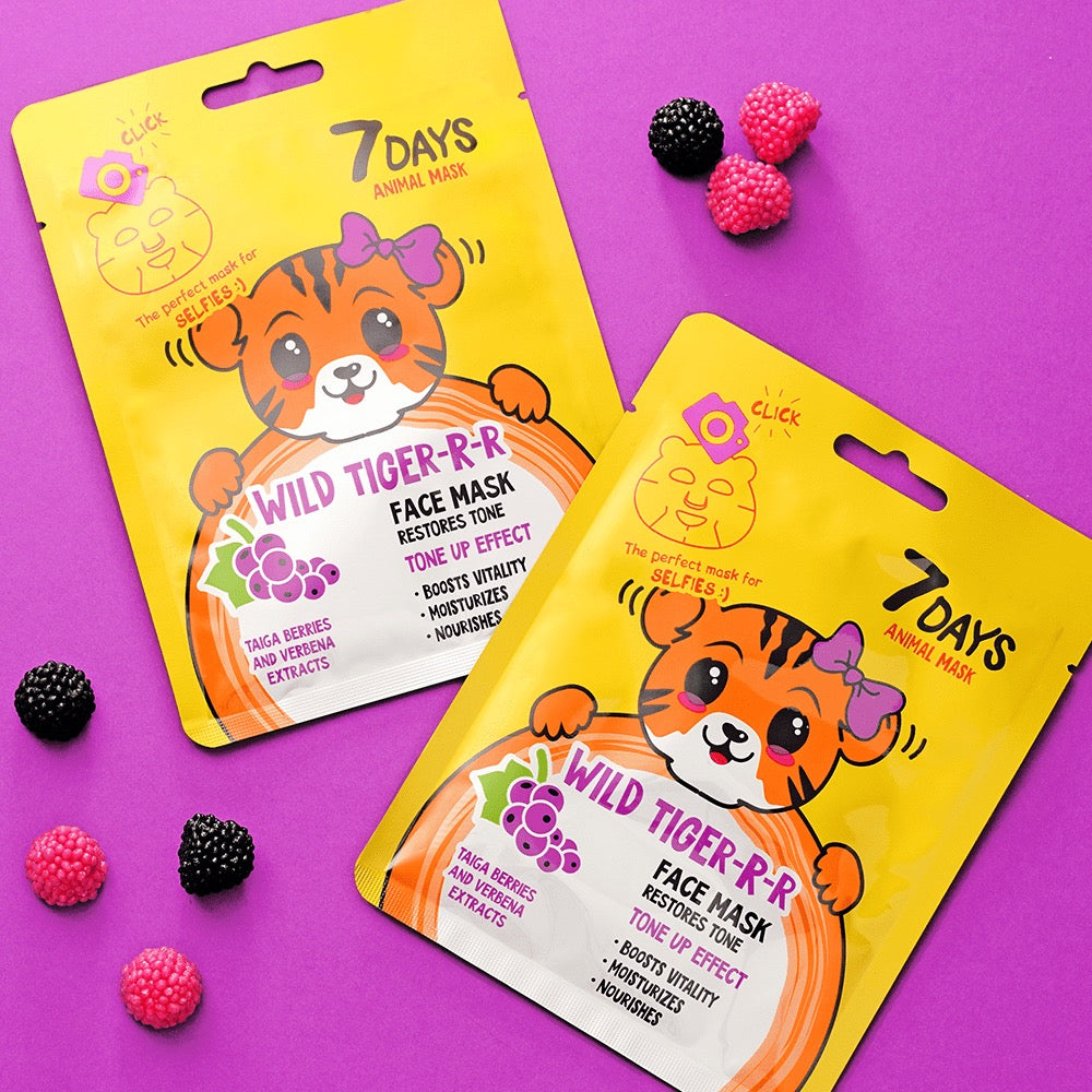 Zwei gelbe Sachets der 7DAYS „Wild Tiger-R-R“ Animal Face Mask mit Tiger-Illustration und lila Schleife, auf violettem Hintergrund mit dekorativen Gummibärchen in Beerenform.