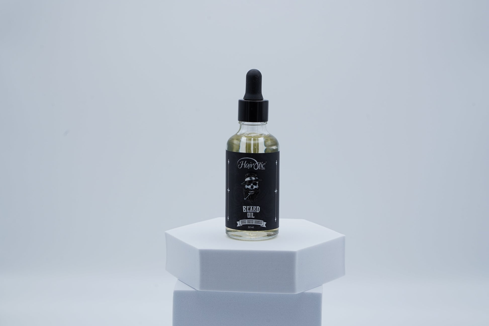 Glasflasche Hairotic Beard Oil mit schwarzem Etikett und Pipettenverschluss, präsentiert auf weißem Podest vor neutralem Hintergrund.