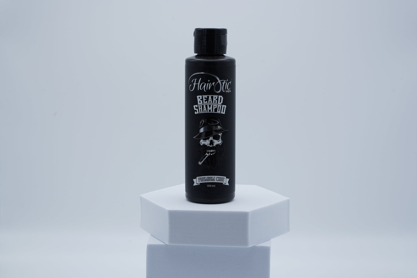 Schwarze Flasche Hairotic Beard Shampoo mit Totenkopf-Logo, stehend auf weißem Podest vor neutralem Hintergrund.
