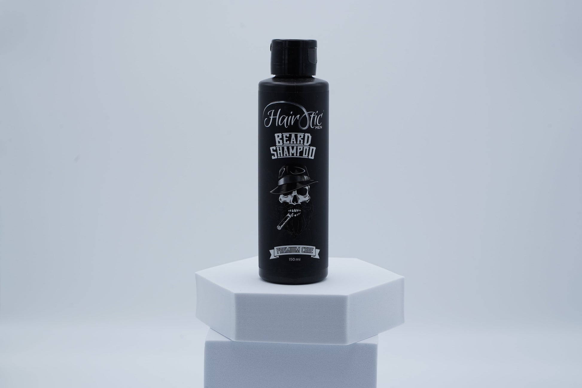 Schwarze Flasche Hairotic Beard Shampoo mit Totenkopf-Logo, stehend auf weißem Podest vor neutralem Hintergrund.