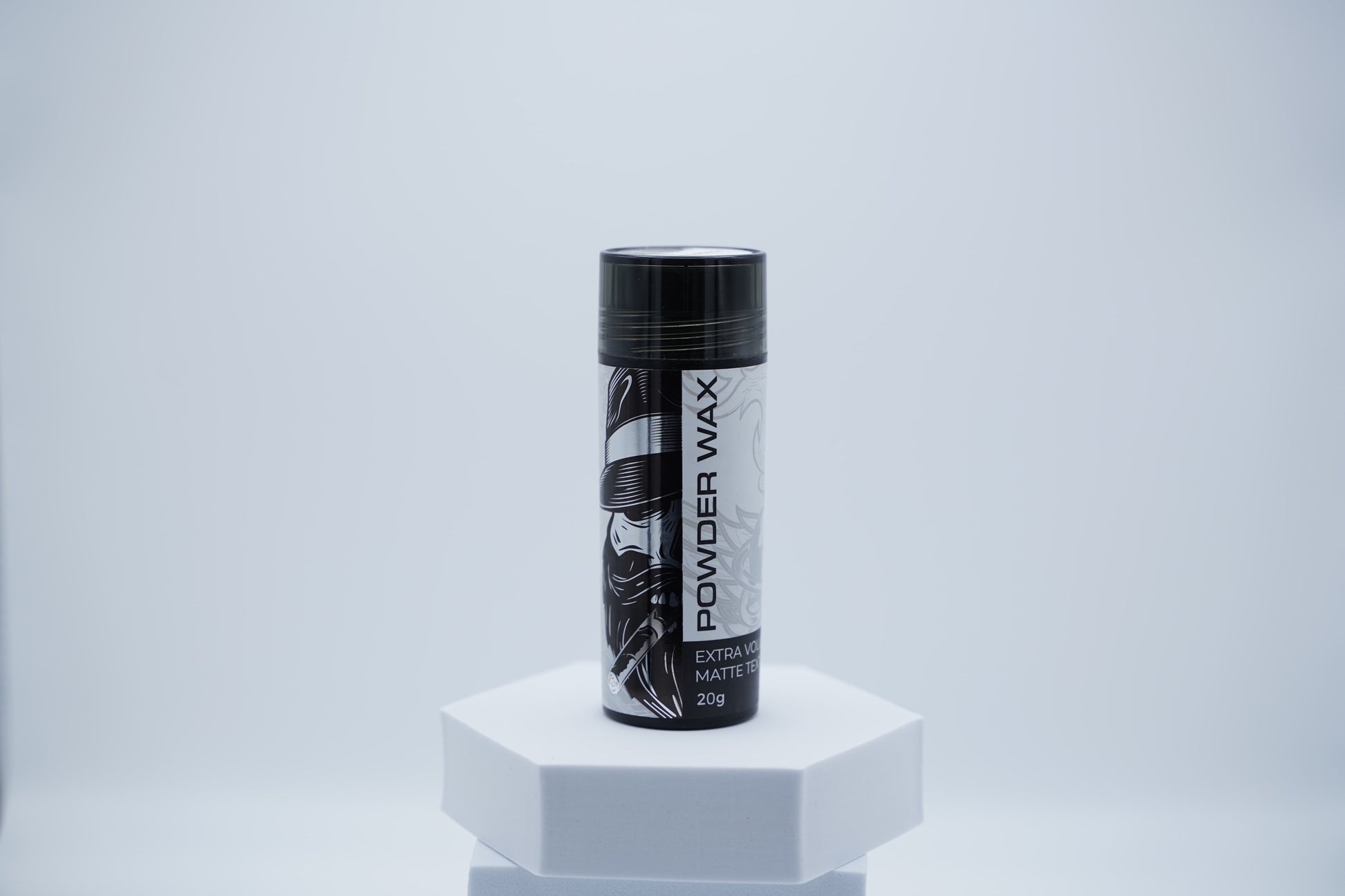 Schwarze Dose Hairotic Powder Wax mit weiß-schwarzem Etikett für extra Volumen und mattes Finish, 20 g, auf weißem Podest vor hellem Hintergrund.