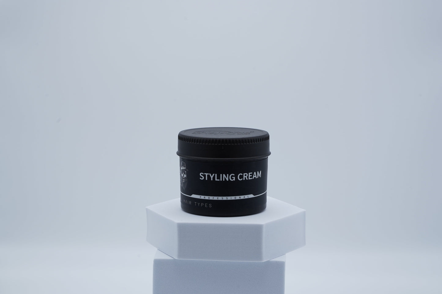 Schwarze Dose Hairotic Styling Cream für alle Haartypen auf weißem Podest, minimalistischer Hintergrund.