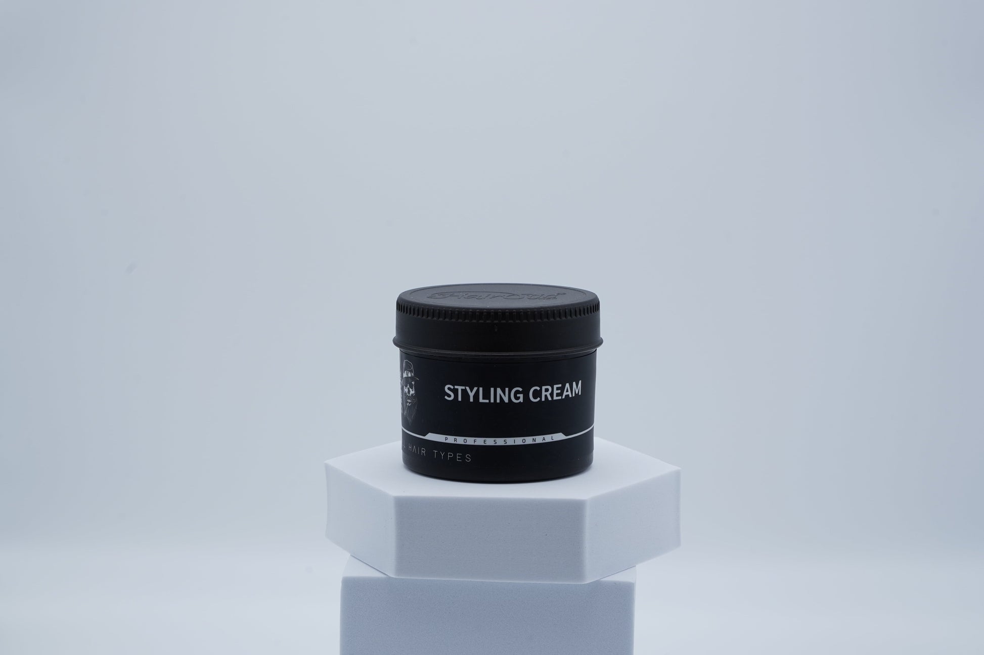 Schwarze Dose Hairotic Styling Cream für alle Haartypen auf weißem Podest, minimalistischer Hintergrund.