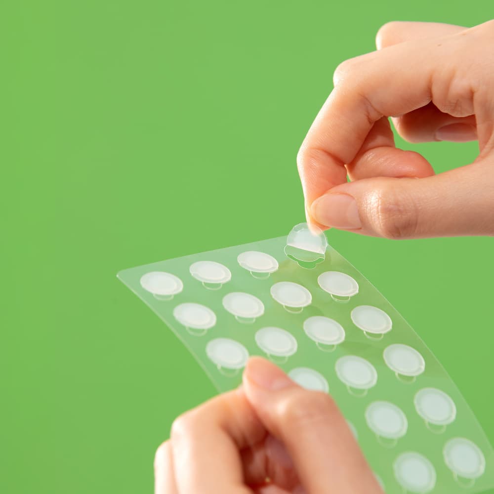 Troubless Invisible Spot Patch – transparente Hydrocolloid-Pflaster auf Trägerfolie, Hand löst ein Patch ab