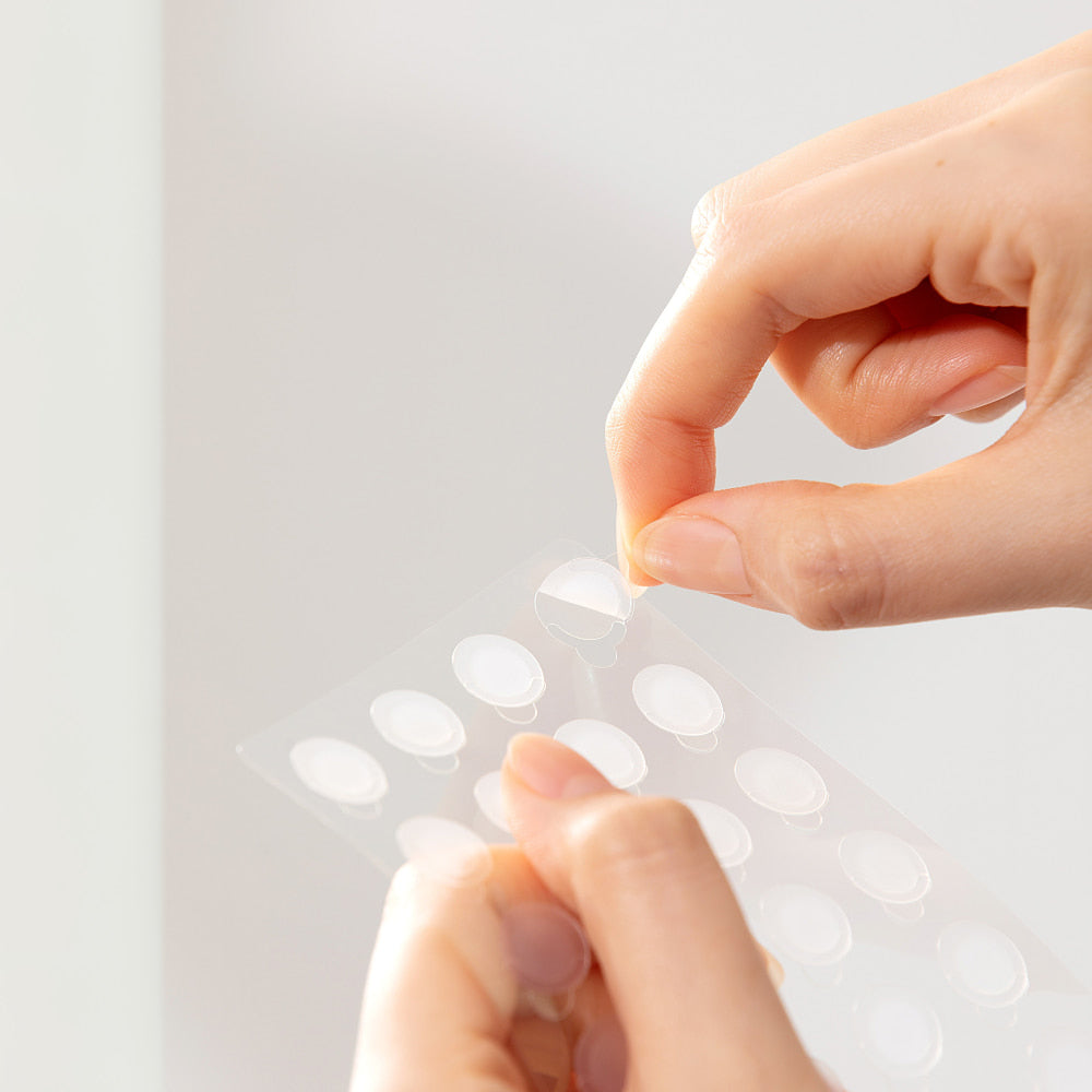 Troubless Invisible Spot Patch Classic – transparente Pflaster auf Folie, Hand löst ein Hydrocolloid-Patch ab
