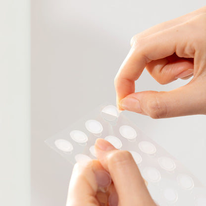 Troubless Invisible Spot Patch Classic – transparente Pflaster auf Folie, Hand löst ein Hydrocolloid-Patch ab